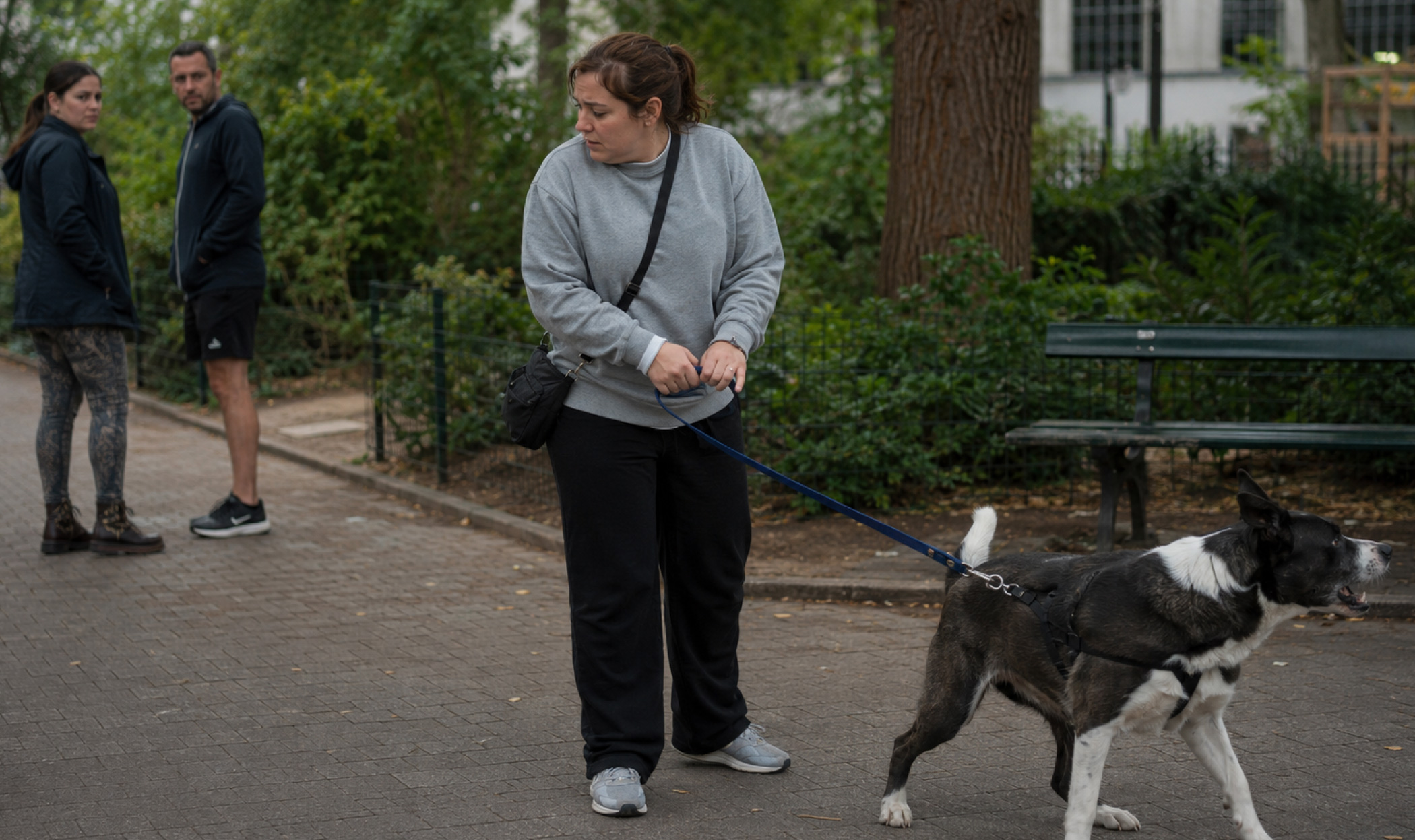 Proprietaria a disagio durante una passeggiata mentre il cane reagisce a uno stimolo e due persone osservano la scena.